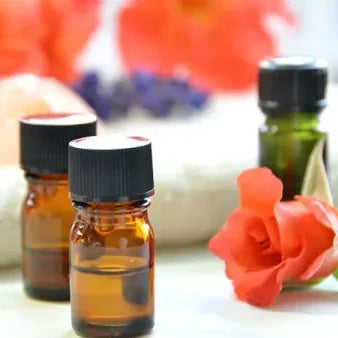 Kleine Glasflaschen mit schwarzen Verschlüssen neben roten Blüten